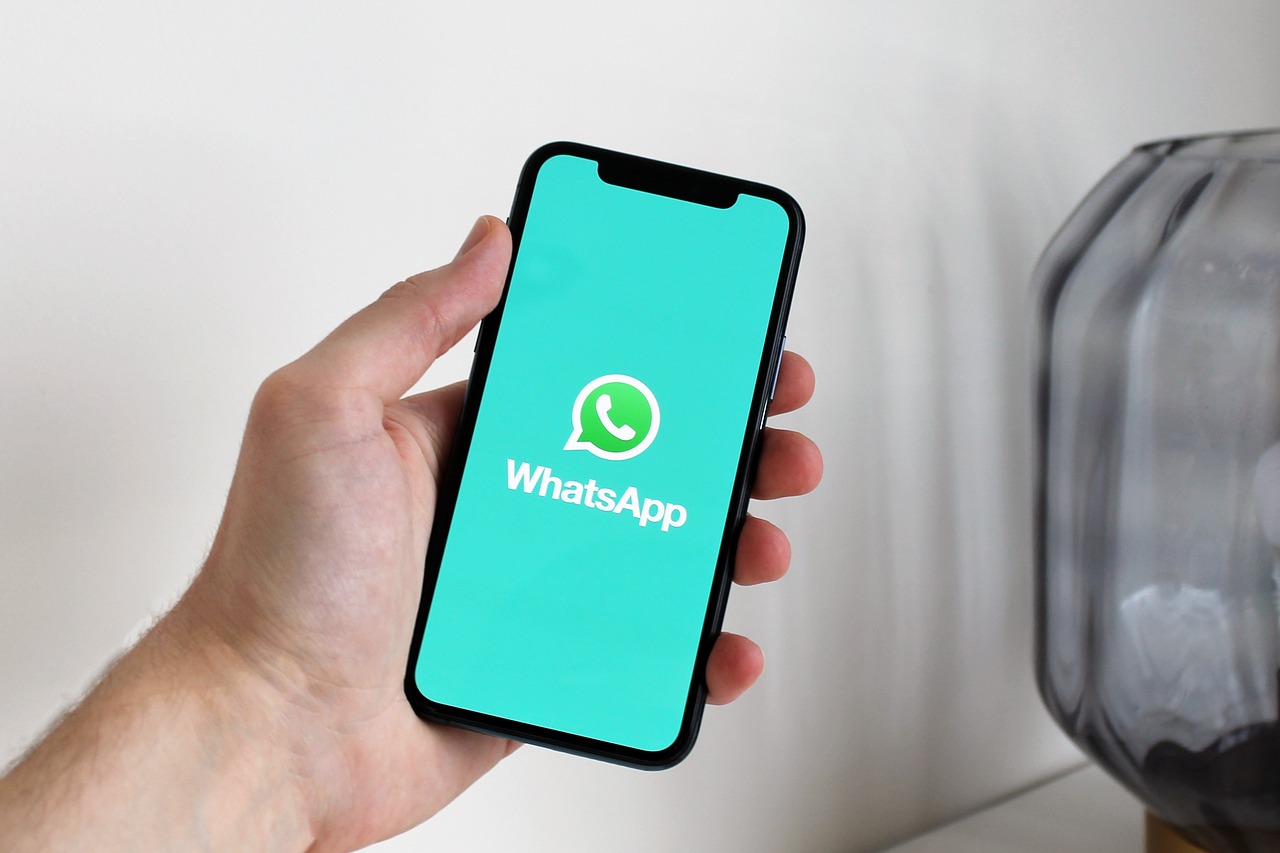 A hand holding a phone showing the WhatsApp launch screen.