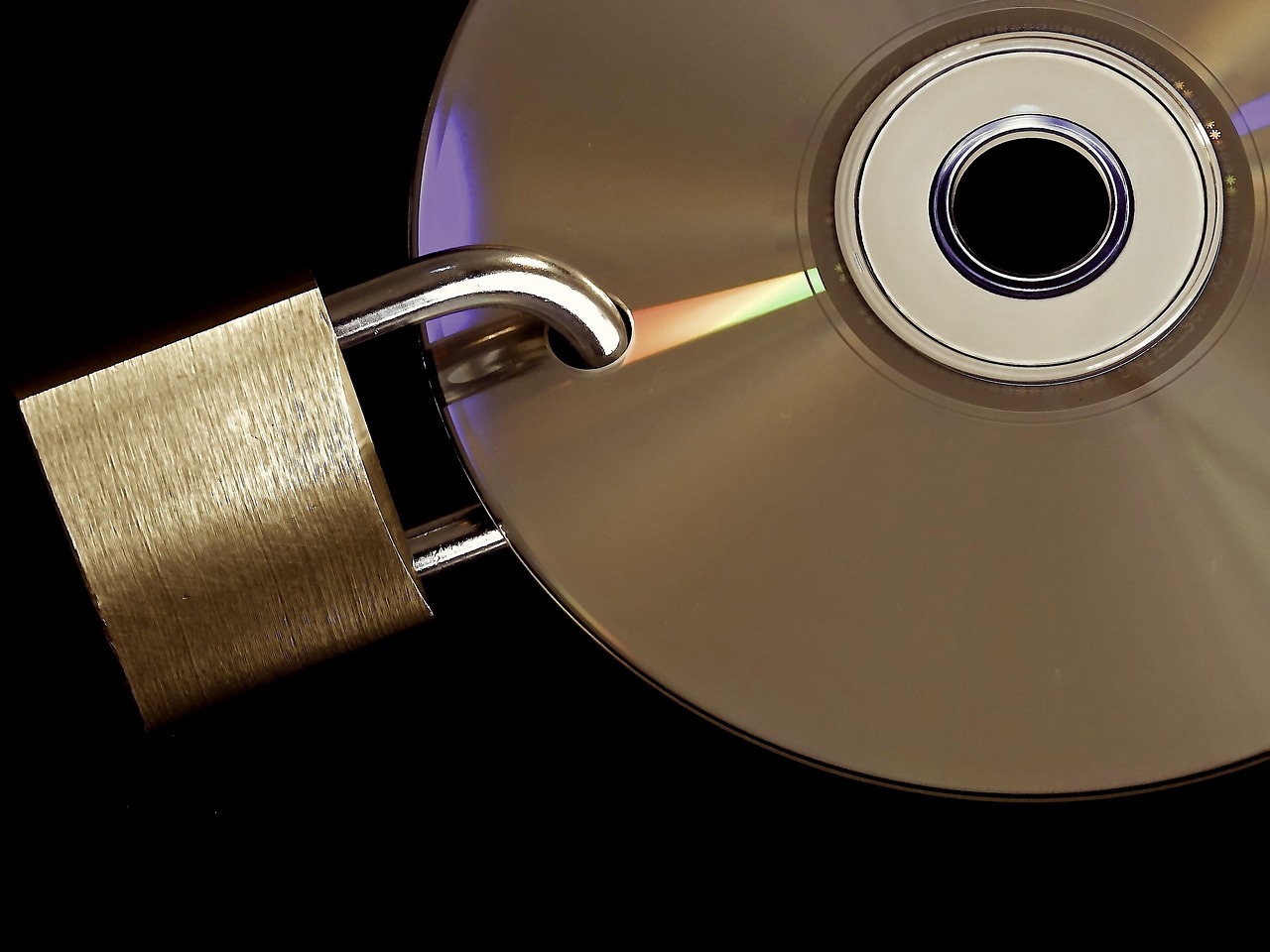 An open brass padlock hooked over the edge of a gold optical disc against a black background