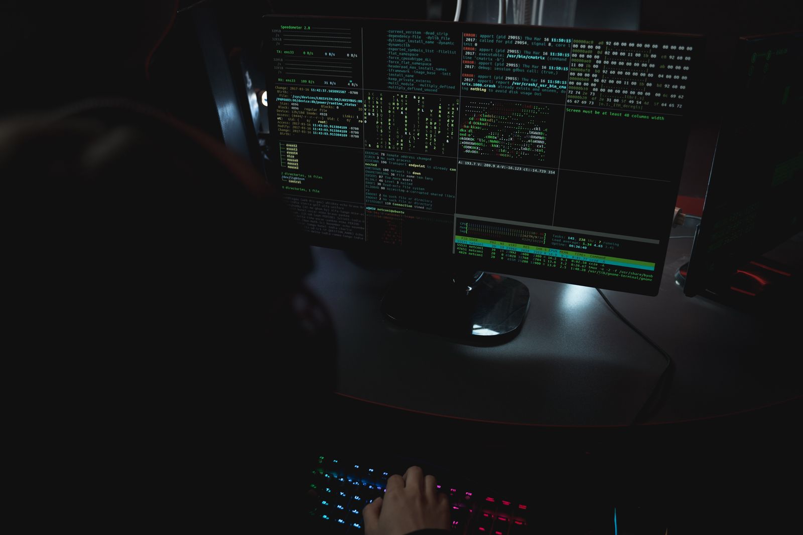 A dark room workstation setup with code displayed on several PC monitors