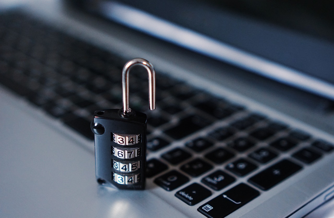 A combination padlock with its shackle open, resting on a laptop keyboard
