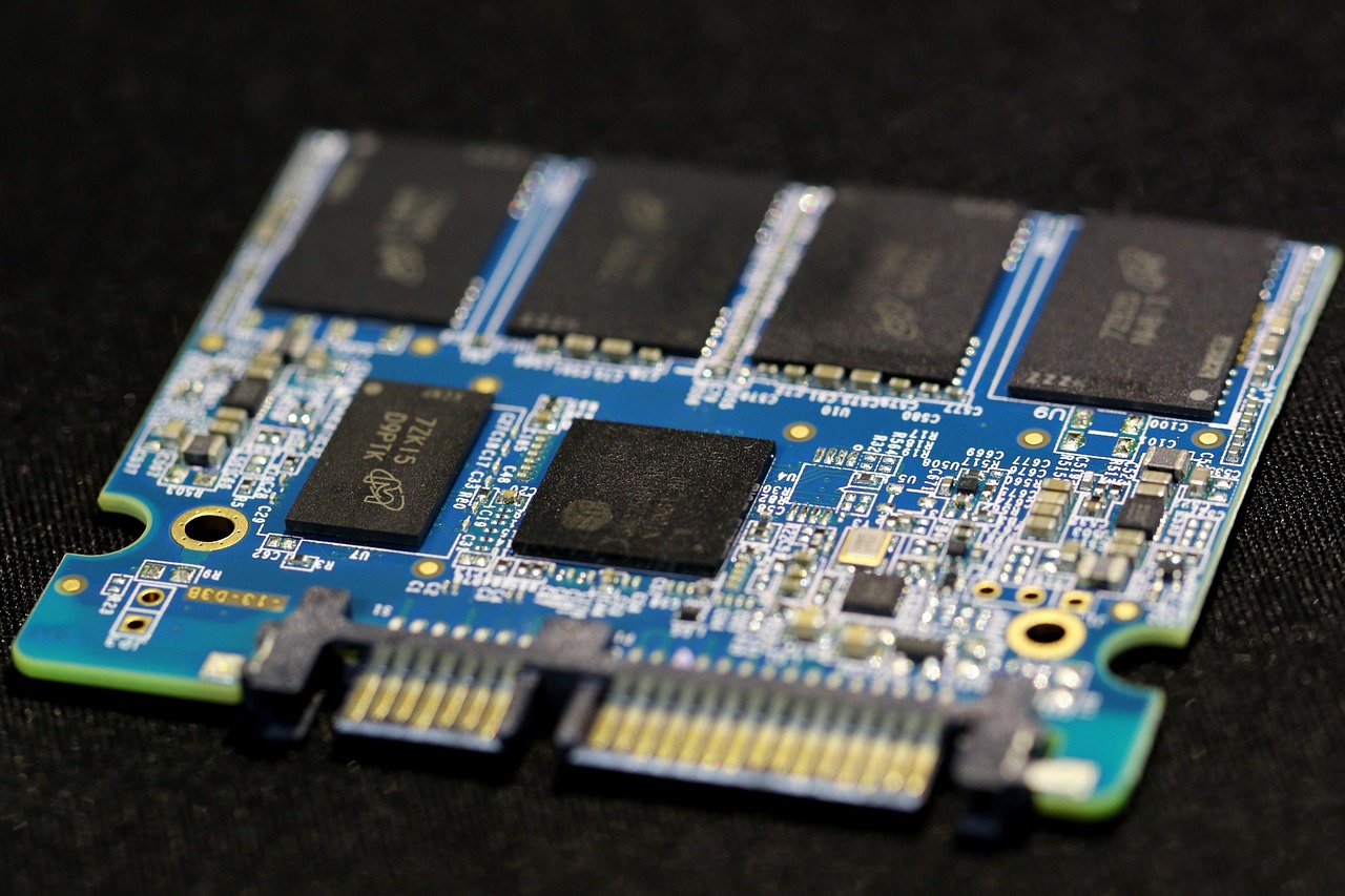 The bare circuit board of a SATA SSD showing its black NAND flash memory chips and gold edge connector
