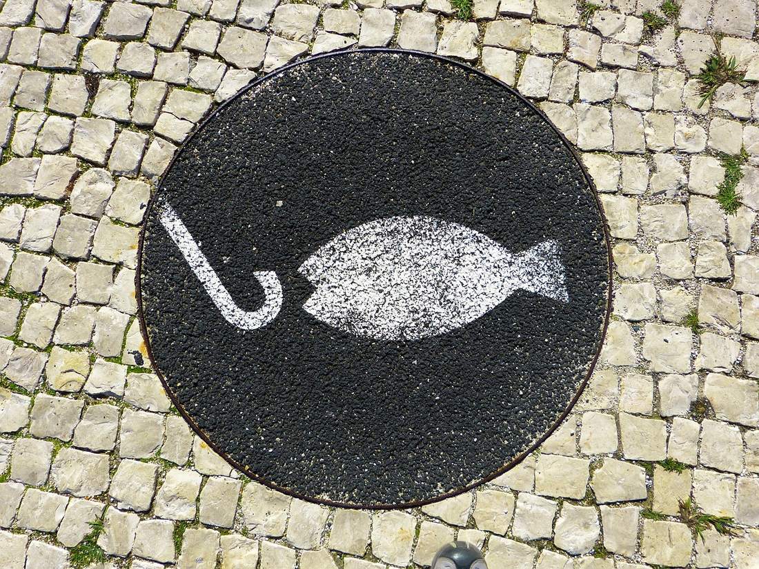 A painted symbol of a fish and a hook on a circular sign set in cobblestones